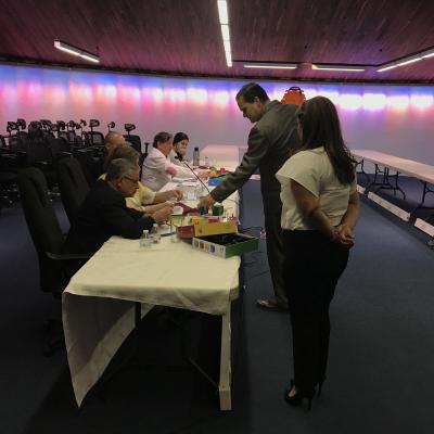 hombre de pie habla con personas que están sentadas en una mesa larga