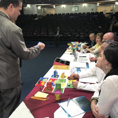 hombre de pie habla con cinco personas sentadas en mesa larga