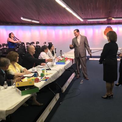 hombre de pie habla con cinco personas sentadas en mesa larga