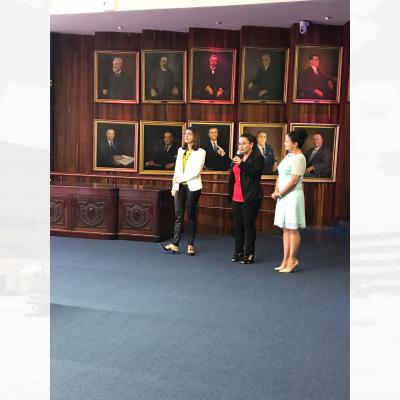  tres mujeres de pie, la del centro hablando  con micrófono en mano