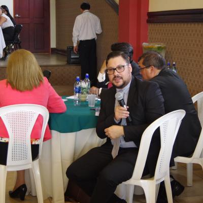 hombre sentado   habla con micrófono en mano 