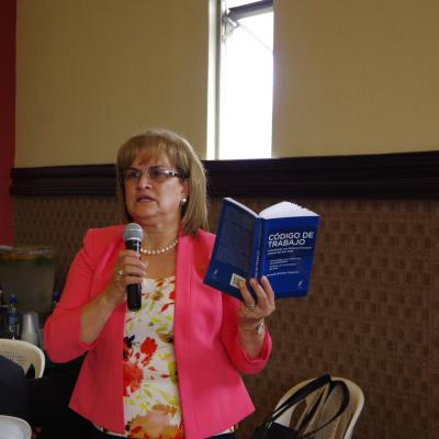 mujer de pie habla con micrófono y libro en mano 