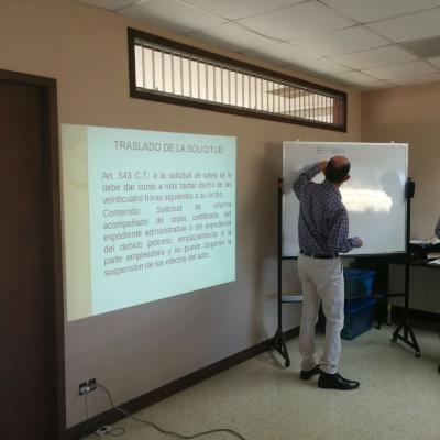 Hombre escribiendo en pizarrón y presentando a compañeros de grupo