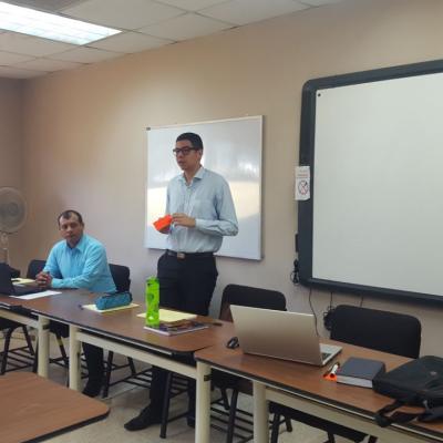 Hombre de pie presentando información con un papel rojo en su mano