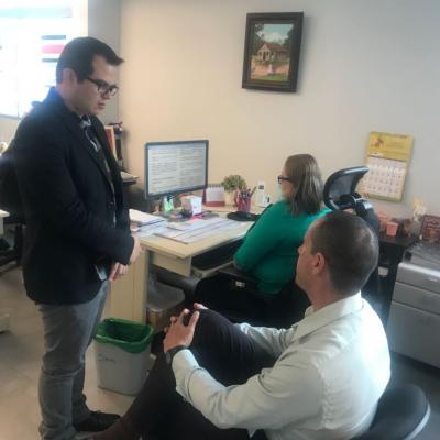 Mujer sentada en su escritorio y dos compañeros detrás conversan