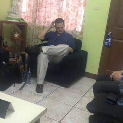 Hombre sentado en sillón leyendo un folleto con dos personas más