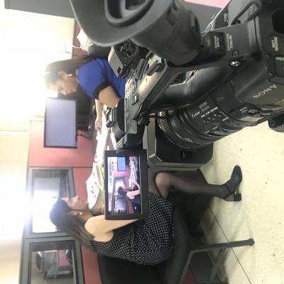 Mujer entrevistando a otra mujer mientras es grabada por cámara de video