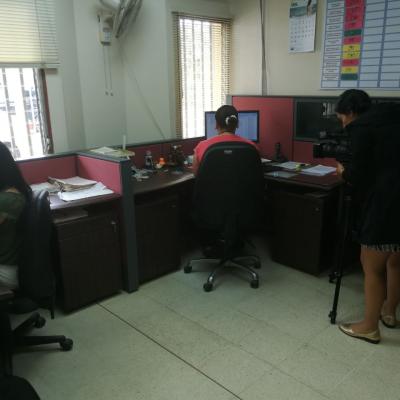 Mujer grabando con cámara de video a otra mujer sentada en su escritorio