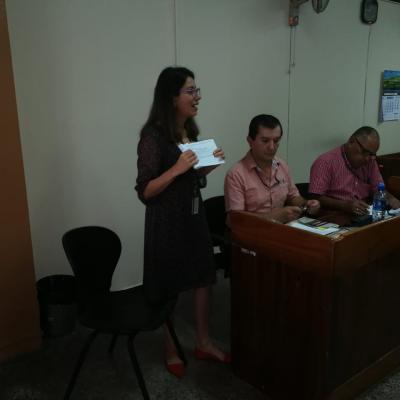Dos hombres de sentados y mujer de pie sosteniendo un documento 