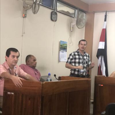 Dos hombres sentados y uno de pie discutiendo 