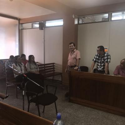 Grupo de personas sentadas y dos hombres de pie en un juzgado