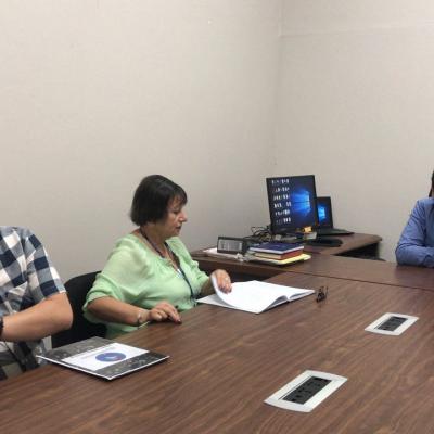 Mujer sentada leyendo folleto en sala de reuniones junto con dos hombres más