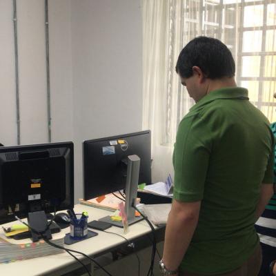 Hombre observando la parte trasera de un monitor junto a mujer y otro hombre