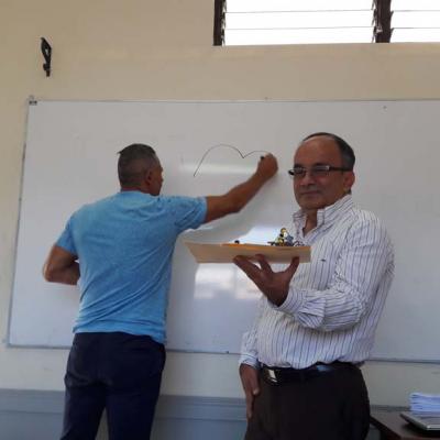 hombre de pie escribiendo en pizarra y otro con maqueta en sus manos