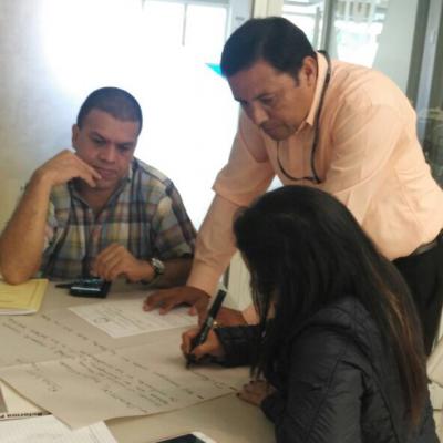 hombre de pie observa el trabajo de dos personas sentadas
