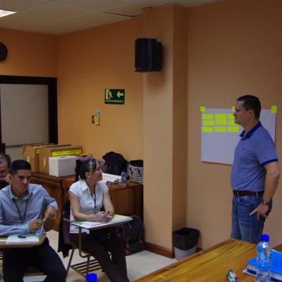 personas sentadas capacitándose y hombre de pie explica
