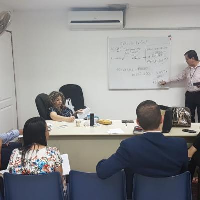 hombre explicando apuntes de pizarra, personas sentadas viéndolo